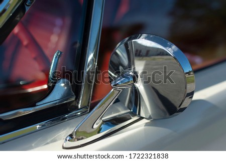 Chrome mirror of an old American muscle car. White classic car with red interior.