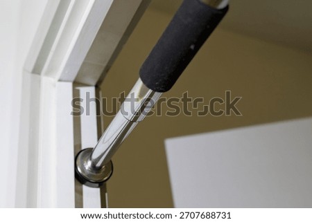 A chrome pull-up bar with a black foam grip is securely installed within a white doorframe, ready for home fitness.