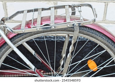 chrome rear rack with fender and part of spoked wheel with orange plastic reflector from women's old iron cherry road classic bicycle near white brick wall during daytime outdoors - Powered by Shutterstock