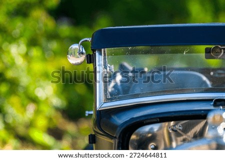 Chrome side mirror and windshield frame on classic roadster closeup