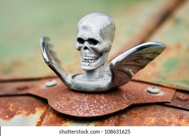 Chrome Skull With Wings Hood Ornament On A Rusty Car