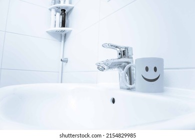 chromed metal faucet for hot and cold water,  cup with smile face for toothbrushes  in a modern bathroom