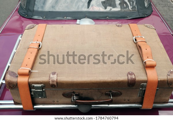 A chromed rear luggage rack with\
an old suitcase and leather belt from a British\
roadster