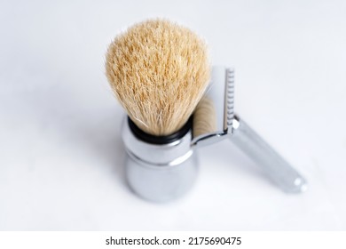 Chrome-plated safety razor and shaving brush isolated on light gray background.