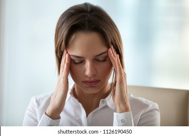 Chronic headache concept, young exhausted woman suffers from migraine touching temples to relieve pain, tired fatigued lady feels dizzy of overwork, stress or hormonal imbalance, headshot, front view