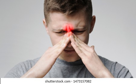 Chronic sinusitis. Young man touching his inflamed hose, close up