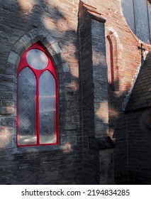 Chruch Red Sice Window With Shadows On The Wall. Side View Os A Red Church Window With A Shadow Os The Cross.