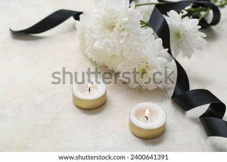 Chrysanthemum flowers with black funeral ribbon and burning candles on light background, closeup