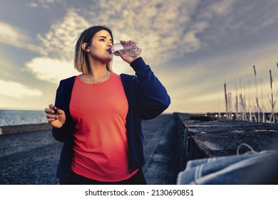 Chubby Athlete Girl Taking A Break From Her Run And Drinking Water From A Plastic Bottle