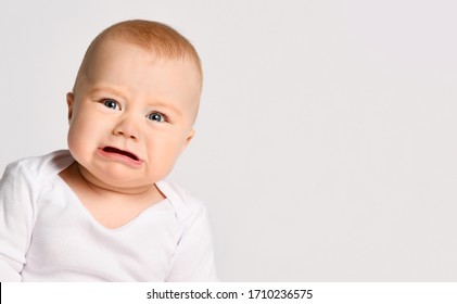 Chubby Little Kid In Bodysuit, Barefoot. He Is About To Cry, Sitting On Floor Isolated On White Studio Background. Concept For Articles About Childhood Or Advertising For Babies. Close Up, Copy Space