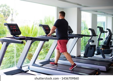 chubby man walking on running track, warming up on gym treadmill. back view.