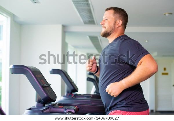 chubby man walking on running track, warming up\
on gym treadmill