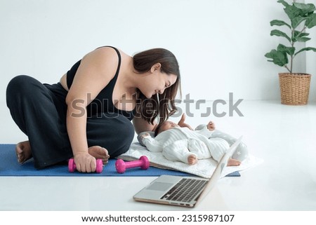 Chubby mom in sportswear pause  her online fitness class on laptop and teasing her baby, doing exercise on floor mat at home
