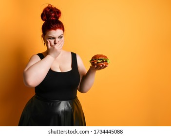 Chubby Overweight Fat Woman Looks With Disgust At Burger Cheeseburger Sandwich With Beef She Holds On Yellow Background With Copy Space. Healthy Eating Diet Fast Food Concept