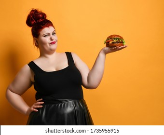 Chubby Overweight Fat Woman Looks Skeptically At Us Holding Burger Cheeseburger Sandwich With Beef On Her Open Palm On Yellow Background. Healthy Eating Diet Fast Food Concept