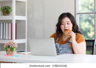 Chubby Woman Eating A Hamburger While Working From Home