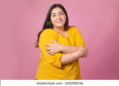 Chubby woman hugging herself transmitting self love with pink background- pretty woman