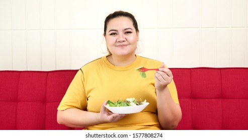 Chubby Woman Sitting On A Sofa And Eating Salad.