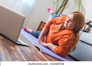 Chubby Woman Sport At Home Lying On Yoga Mat Watching Online Workout Video On Laptop Raising Leg Concentrated