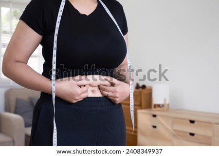 Chubby woman uses a measuring tape to measure her stomach.