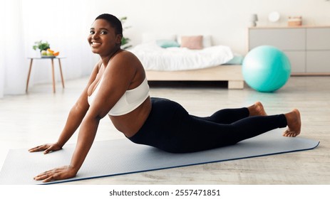 Chubby young black lady stretching on sports mat, practicing yoga, trying to lose weight at home, full length. Plus size African American woman working out during her slimming program - Powered by Shutterstock