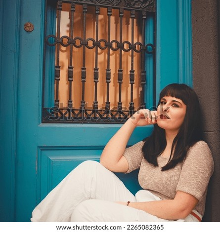 Chubby young cute model girl posing sitdown looking at camera with blue wooden door as background