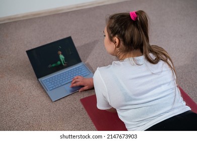 A chubby young woman is watching an online fitness lesson on a laptop. Distance sports training.