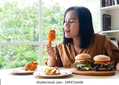 Chuby Woman Eating A Large Piece Of Fried Chicken In The Living Room With A Lot Of Fast Food On The Table. She Stuck Her Tongue Out Of Hunger And Thirst And Stared At The Object With Excitement.