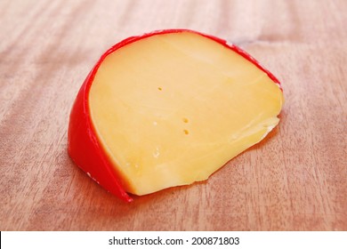 Chunk Of Aged French Cheddar Cheese In Hard Red Shell On Wooden Table