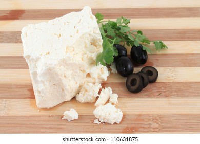 Chunk Of Feta Cheese With Crumbles And Black Olives And Cilantro  On A Wooden Board