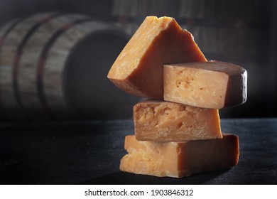 Chunks of hard, perennial cheese against a backdrop of wooden barrels. The cheese is stacked in vertical rows. The concept of still life. Natural dairy product. Copy space. - Powered by Shutterstock