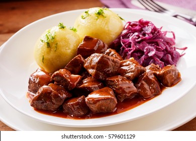 Chunky Beef Stew With Savory Sauce Beside Potato Topped With Herbs And Purple Cabbage