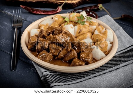 Chunky beef stew with savory sauce beside potato dumplings.