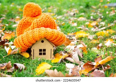 Chunky pompon hat placed on a small toy house on a green lawn covered with pigmented autumn leaves. - Powered by Shutterstock