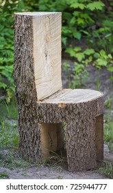 Chunky Ugly Chair Made Of The Whole Tree Trunk Is Standing Outdoor On The Ground. Unfocused Green Forest Background.