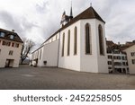 Church in Aarau old town. Big paved place in the foreground. Cloudy sky. Bare tree.