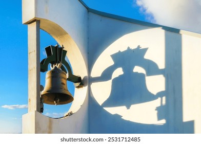 Church Bell Casting Dramatic Shadow on Modern White Bell Tower Against Blue Sky