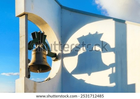 Church Bell Casting Dramatic Shadow on Modern White Bell Tower Against Blue Sky