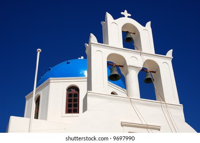 The church bells and blue dome of a greek building stand out on the dark blue sky.