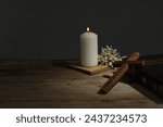 Church candle, flowers, cross and Bible on wooden table, space for text