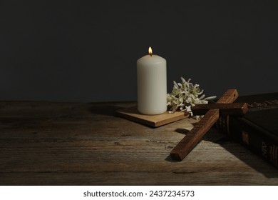 Church candle, flowers, cross and Bible on wooden table, space for text