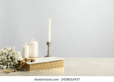 Church candles, wooden cross, rosary beads, Bible and flowers on light table. Space for text