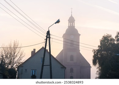 Church and house silhouette against misty dawn sky with utility pole and wires on a quiet morning. Rural infrastructure creating a picturesque atmosphere. High quality photo - Powered by Shutterstock