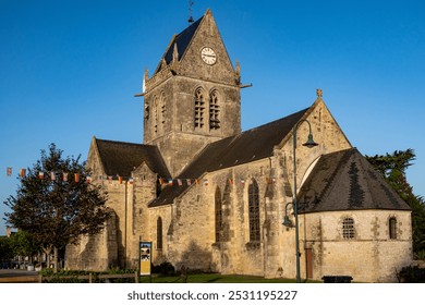 Sainte-Mère-Église Church in Normandy, France, with D-Day flags and iconic clock tower. Captures historic Gothic architecture and commemorates World War II Allied bravery and liberation. - Powered by Shutterstock