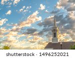 Church steeple and roof viewed against blue sky and puffy clouds on a sunny day