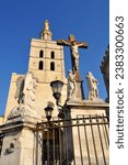 Church tower with statues and cross with jesus at papal palace in Avignon, France.