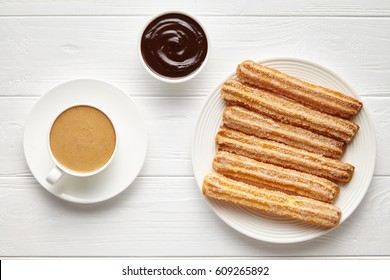 Churros Traditional Homemade Spain Street Fast Food Baked Sweet Dough Snack With Chocolate And Coffee, White Plate, White Table Background. Flat Lay Top View