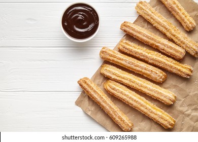 Churros Traditional Spain Street Fast Food Baked Sweet Dough Snack With Chocolate, Rustic Decorative Paper, White Table Background. Flat Lay Top View