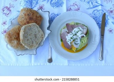 Ciabatta, Italian Bread Buns. Plate With Ciabatta Sandwich Bread With Smoked Ham And Poached Egg.  Bowl With Home Baked Burger Buns, One Piece Of Ciabatta Bread With Leeks Cut In Half. 