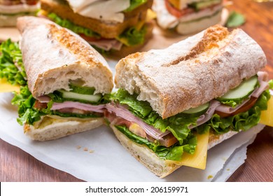 Ciabatta Sandwich with mustard, lettuce, slices of fresh tomatoes, ham, and cheese cut in half
